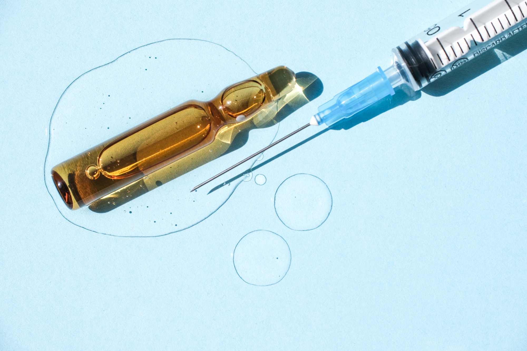 Ampoule, injection syringe and a drop of cosmetic gel on a blue background.