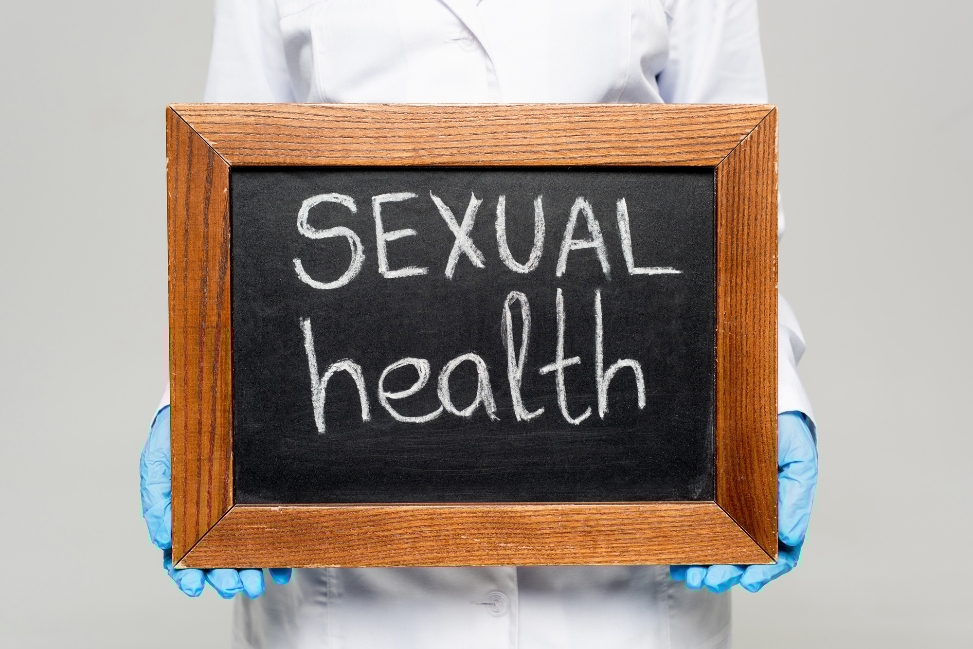 cropped view of doctor in white coat and latex gloves holding chalkboard with sexual health