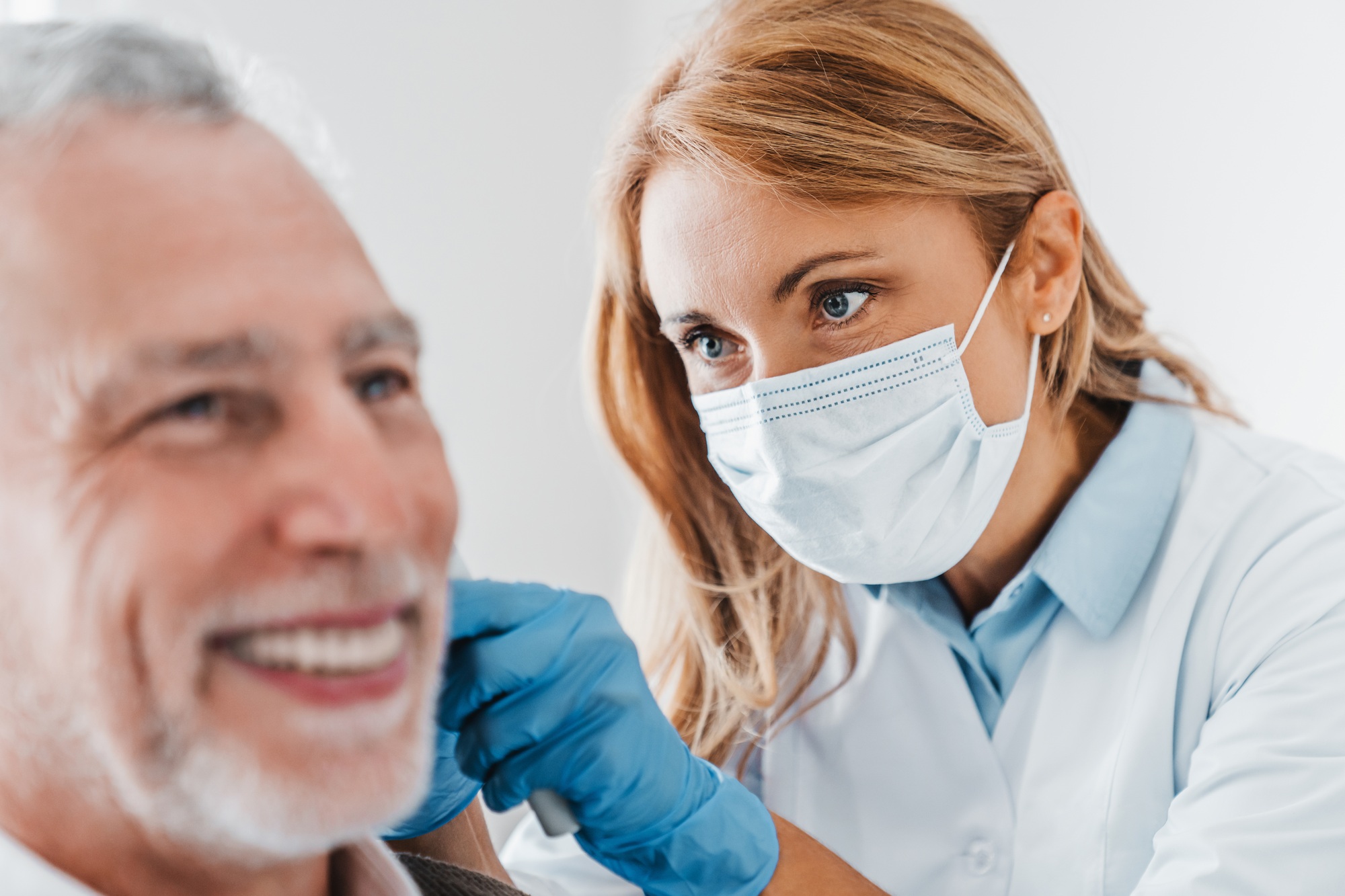 Doctor checking ear of elderly man using otoscope